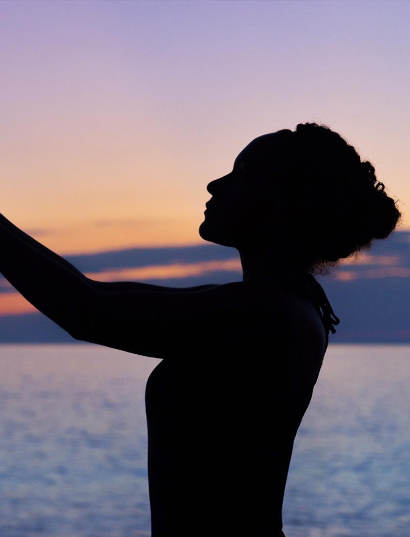 A woman standing on the beach at sunset.