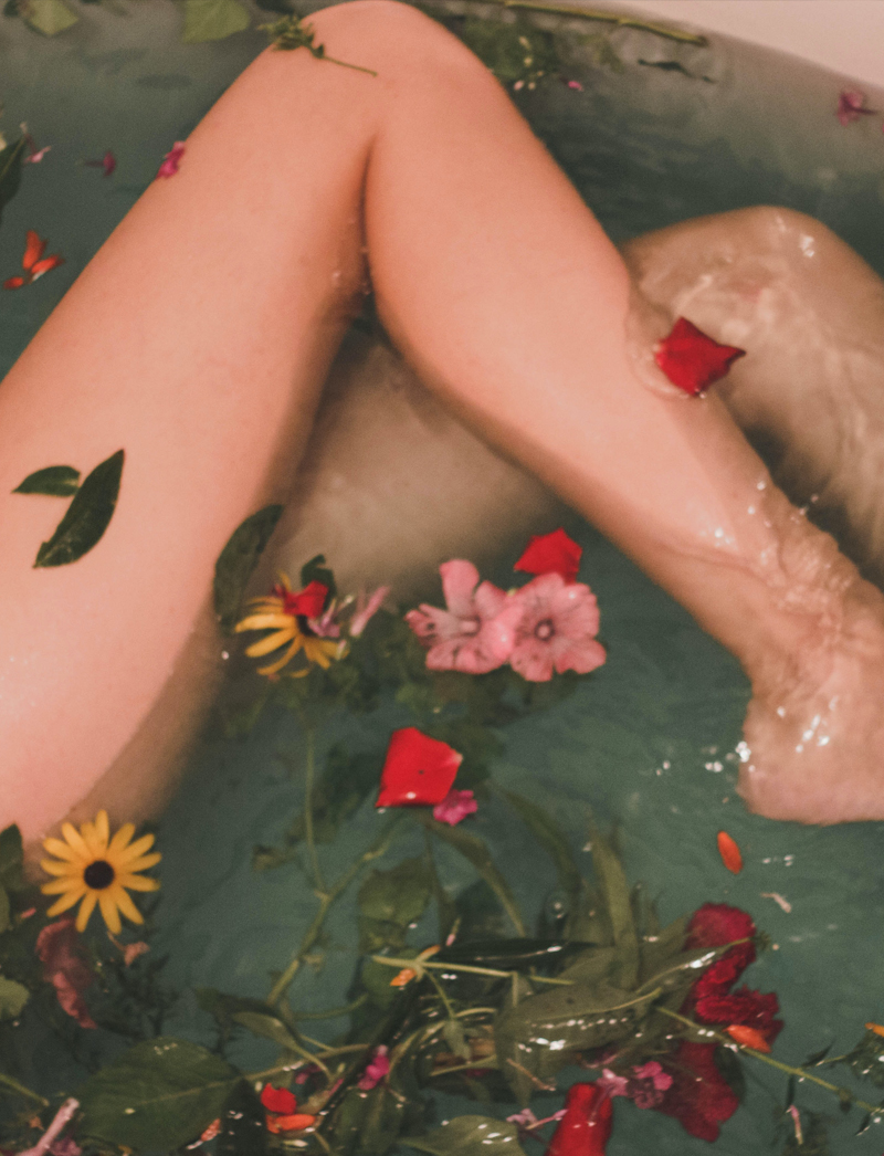 Woman legs in the water with flowers and leaves inside
