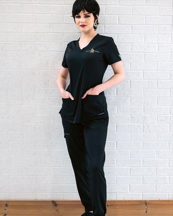 A woman in black scrubs standing next to a wall.